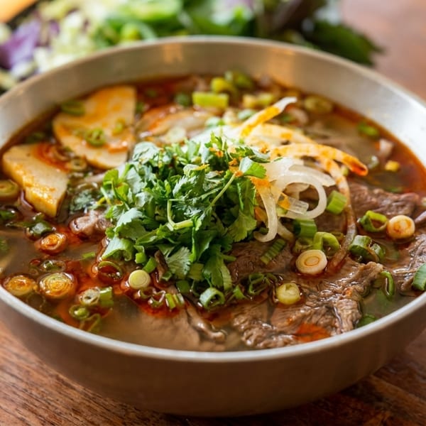 A bowl of Vietnamese pho with beef, noodles, herbs, and broth on a wooden table.