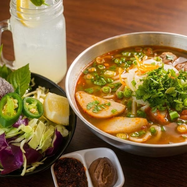 Spicy Vietnamese noodle soup with beef, fish cakes, herbs, and a side of fresh vegetables.